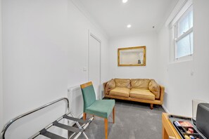 Una habitación pequeña y bien iluminada con una silla verde, un sofá marrón y una mesita de madera con un objeto negro encima.