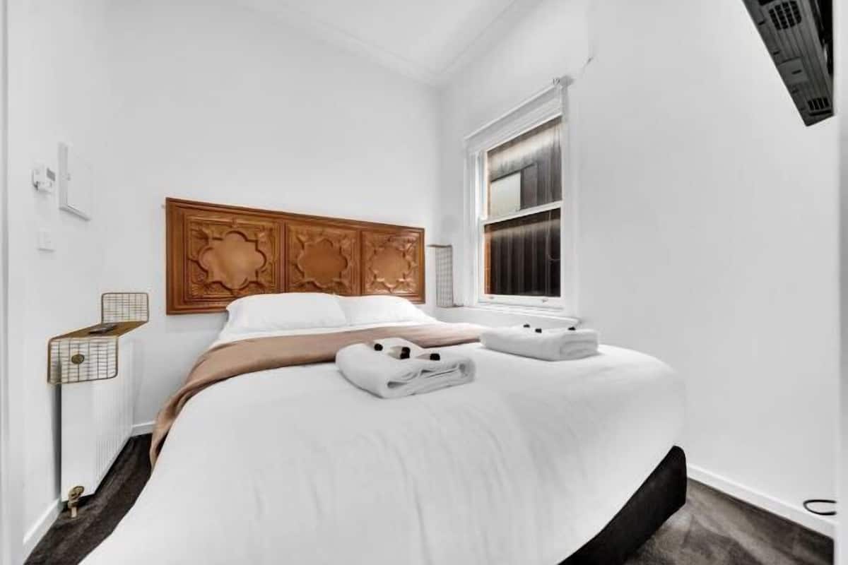 Quarto de hotel com cama, cabeceira de madeira, janela e radiador.