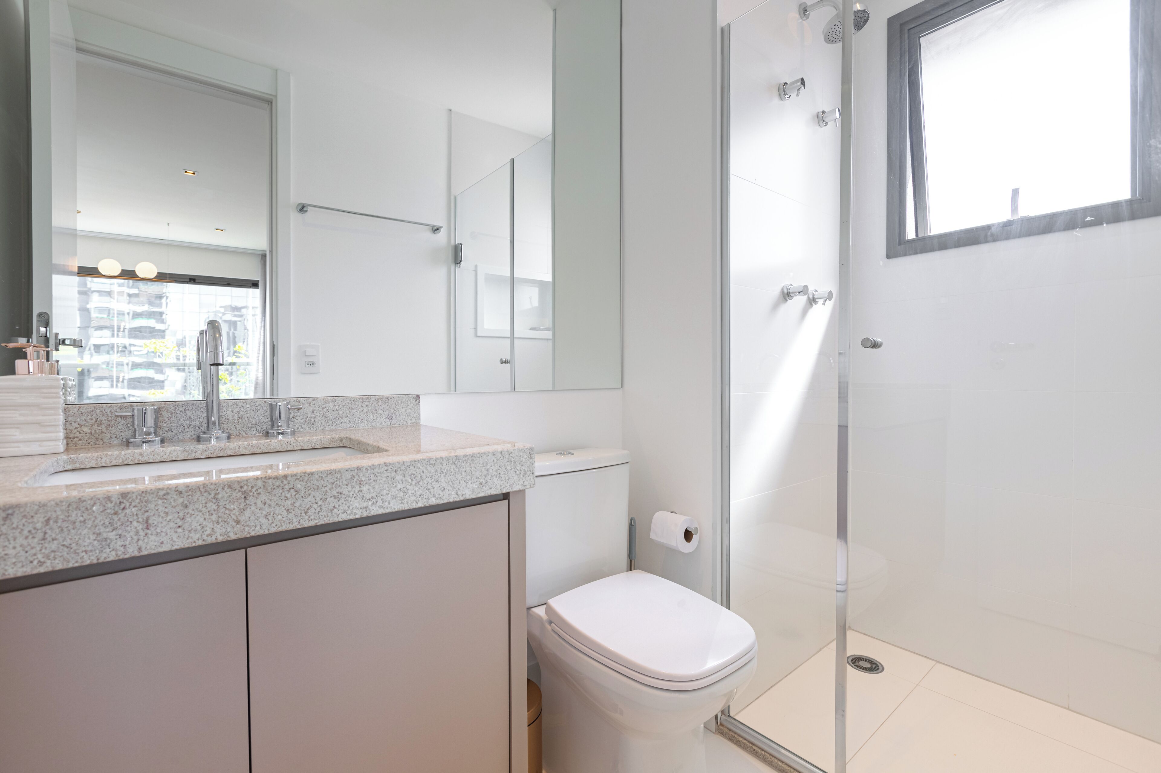 Une salle de bain moderne avec une douche à parois de verre, des toilettes blanches et un plan de toilette en granit avec un lavabo.