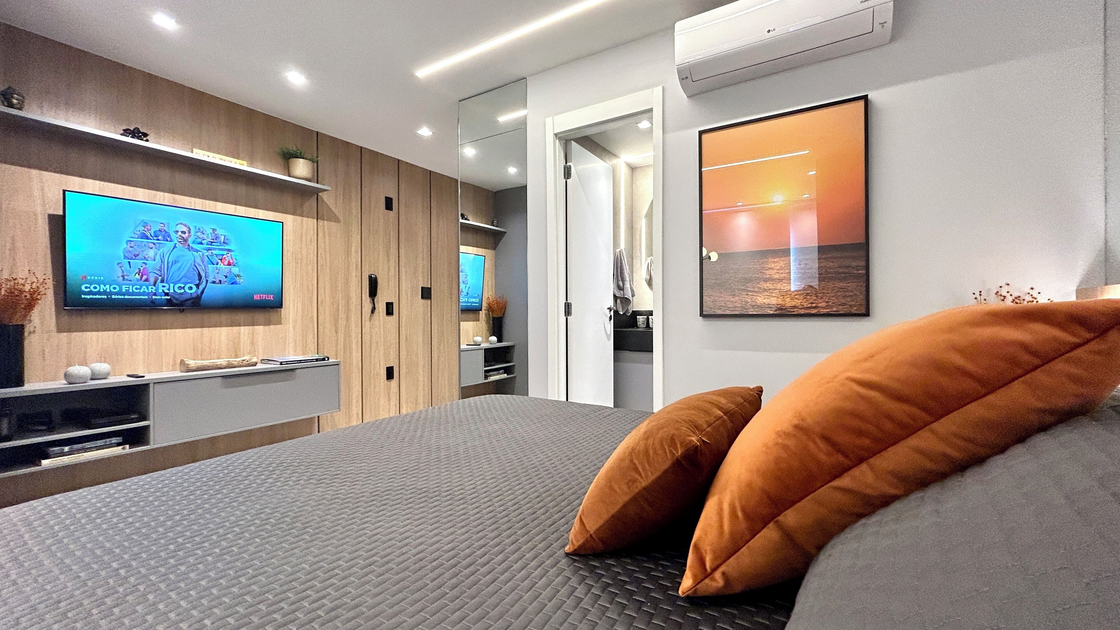 A modern bedroom with a large bed, a TV mounted on the wall, and a framed picture.