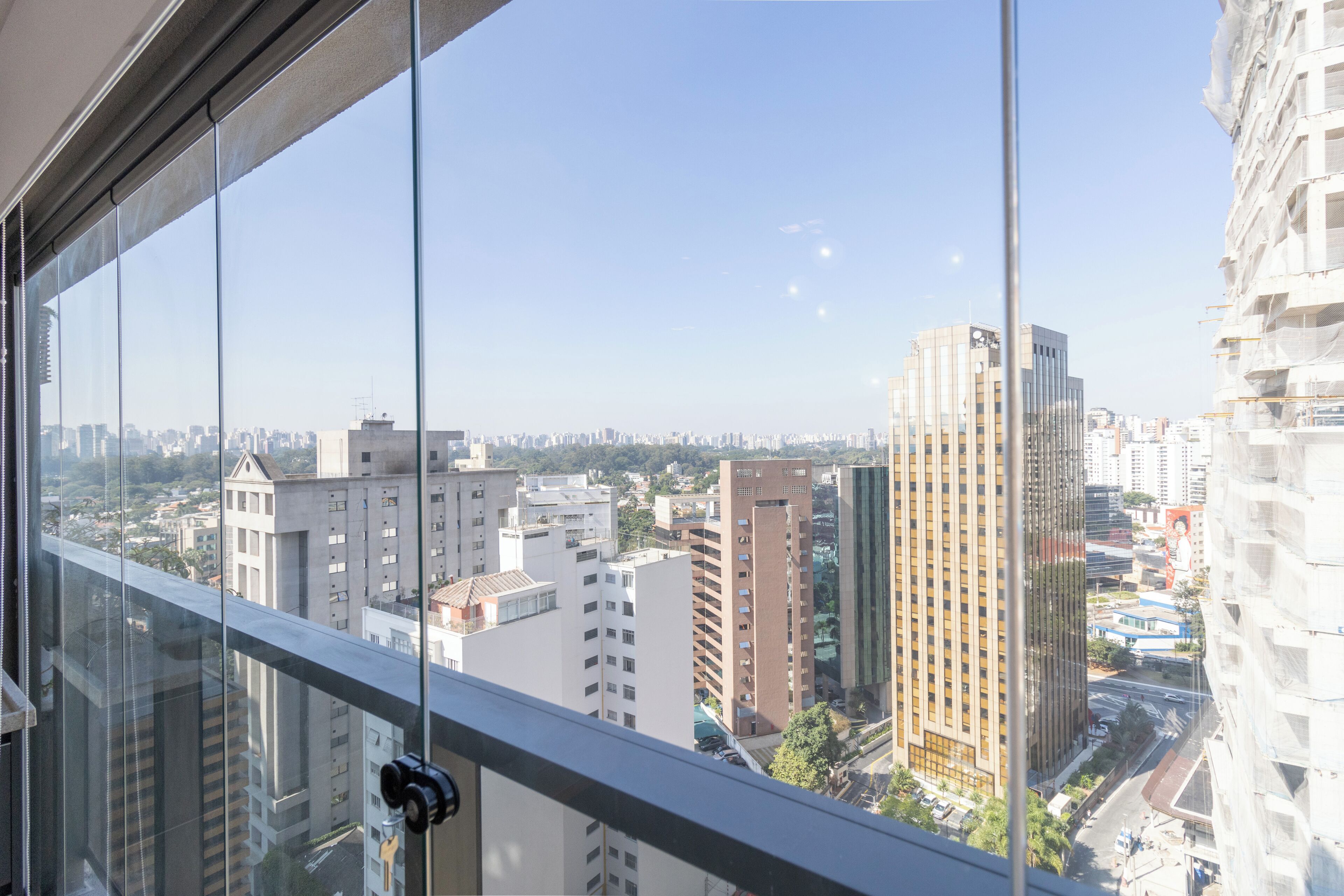 A cityscape through a window with modern buildings, a clear sky, and a street below.