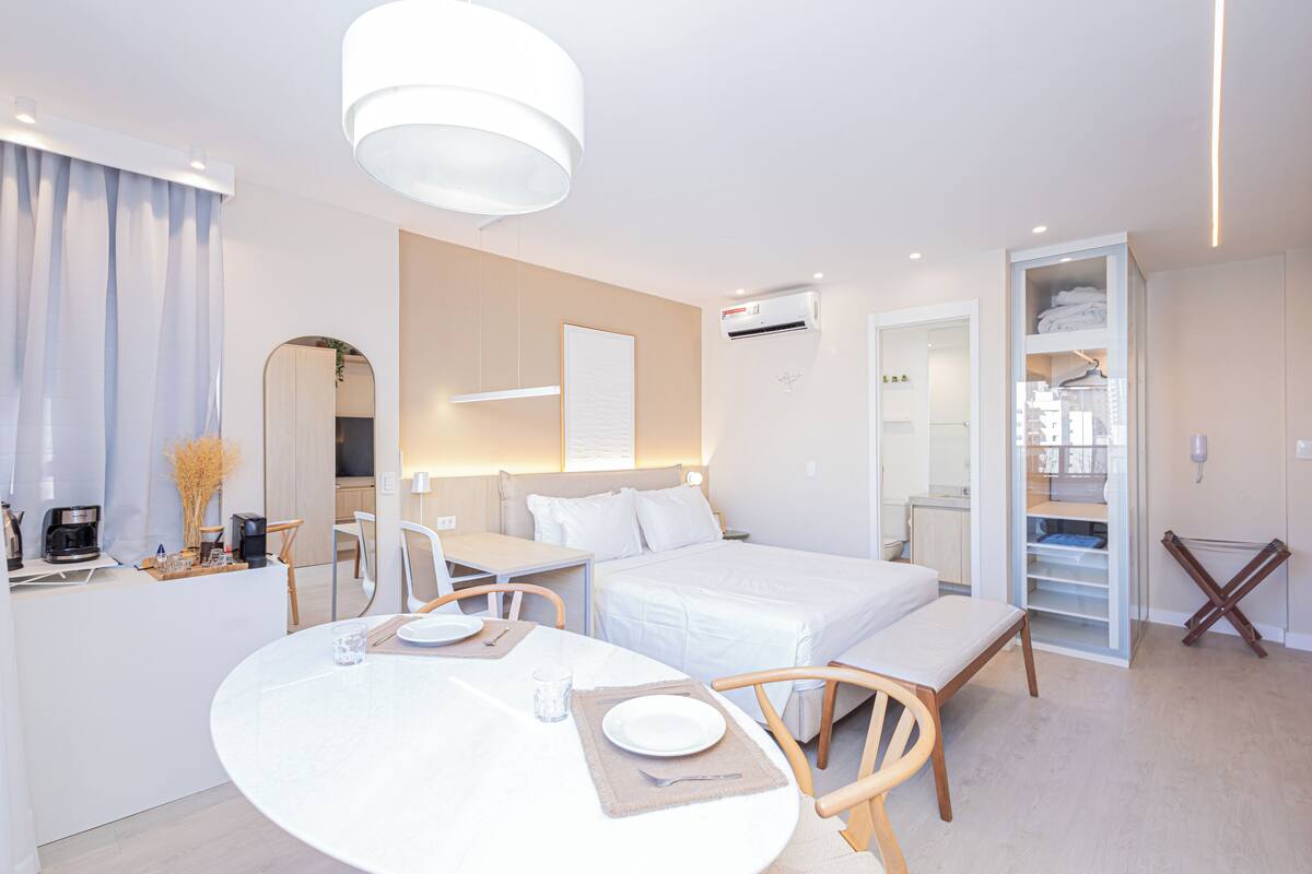 Moderni hotellihuone, jossa on sänky, yöpöytä sekä ruokailualue pöytineen ja tuoleineen.