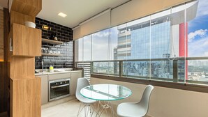 Une cuisine moderne avec une table et des chaises en verre, un four encastré et une vue sur le paysage urbain grâce à de grandes fenêtres.