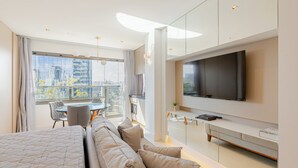 Une chambre d’hôtel moderne dotée d’un grand lit, d’un coin salon avec une table et des chaises, d’un téléviseur à écran plat fixé au mur et d’un balcon offrant une vue sur la ville.