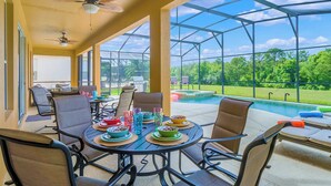 Une terrasse extérieure avec une table dressée pour le repas, des chaises et une piscine en arrière-plan.