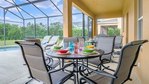 Une terrasse extérieure dotée d’une véranda en verre, de tables avec des chaises, et d’une piscine en arrière-plan.