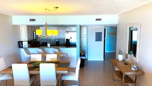 Une cuisine moderne avec des meubles blancs, un îlot central et un coin repas comprenant des chaises blanches et une table en bois.