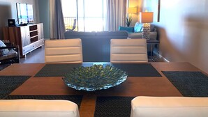 Un salon moderne comprenant une table à manger, deux chaises blanches, un canapé, un téléviseur et un ventilateur de plafond.