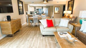A modern living room with a sofa, coffee table, and a dining area with chairs and a table.
