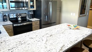 A modern kitchen with stainless steel appliances, granite countertops, and light-colored cabinetry.