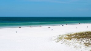 A wide, white sandy beach with clear turquoise water and a few people scattered along the shore.