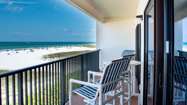 Ein Balkon mit Blick auf Strand und Meer. Zwei gestreifte Stühle und ein kleiner Tisch sind vorhanden.
