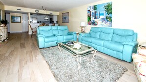 Ein Wohnzimmer mit blauem Sofa, einem Glastisch und einem gemusterten Teppich.