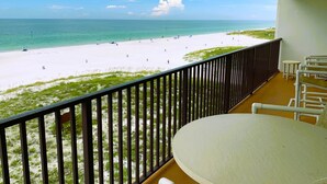Un balcon donnant sur une plage, une table blanche et une chaise.