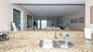 Cocina con encimeras de granito, un lavabo de acero inoxidable y vistas al océano a través de una puerta corrediza de vidrio.