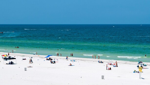 Una playa con arena blanca, agua turquesa cristalina y algunas sombrillas.