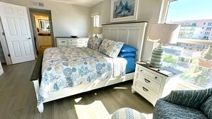 Un dormitorio con cama, mesita de noche, lámpara, ventana con vistas y puerta.