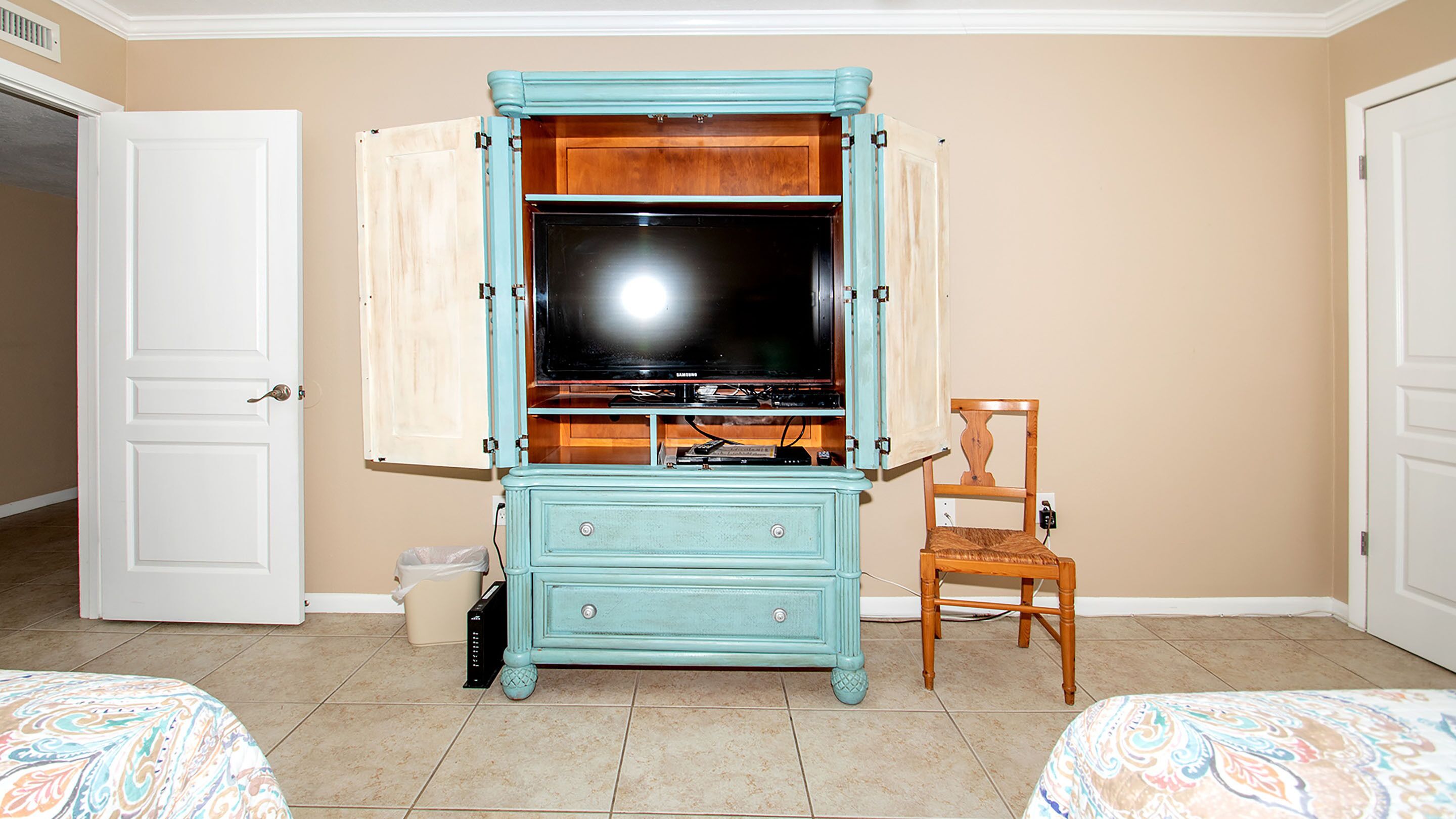 Una habitación con una televisión sobre un mueble de madera, una silla y dos camas.