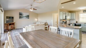 Un salón espacioso con una mesa de comedor de madera, sillas blancas, un sofá y una televisión.