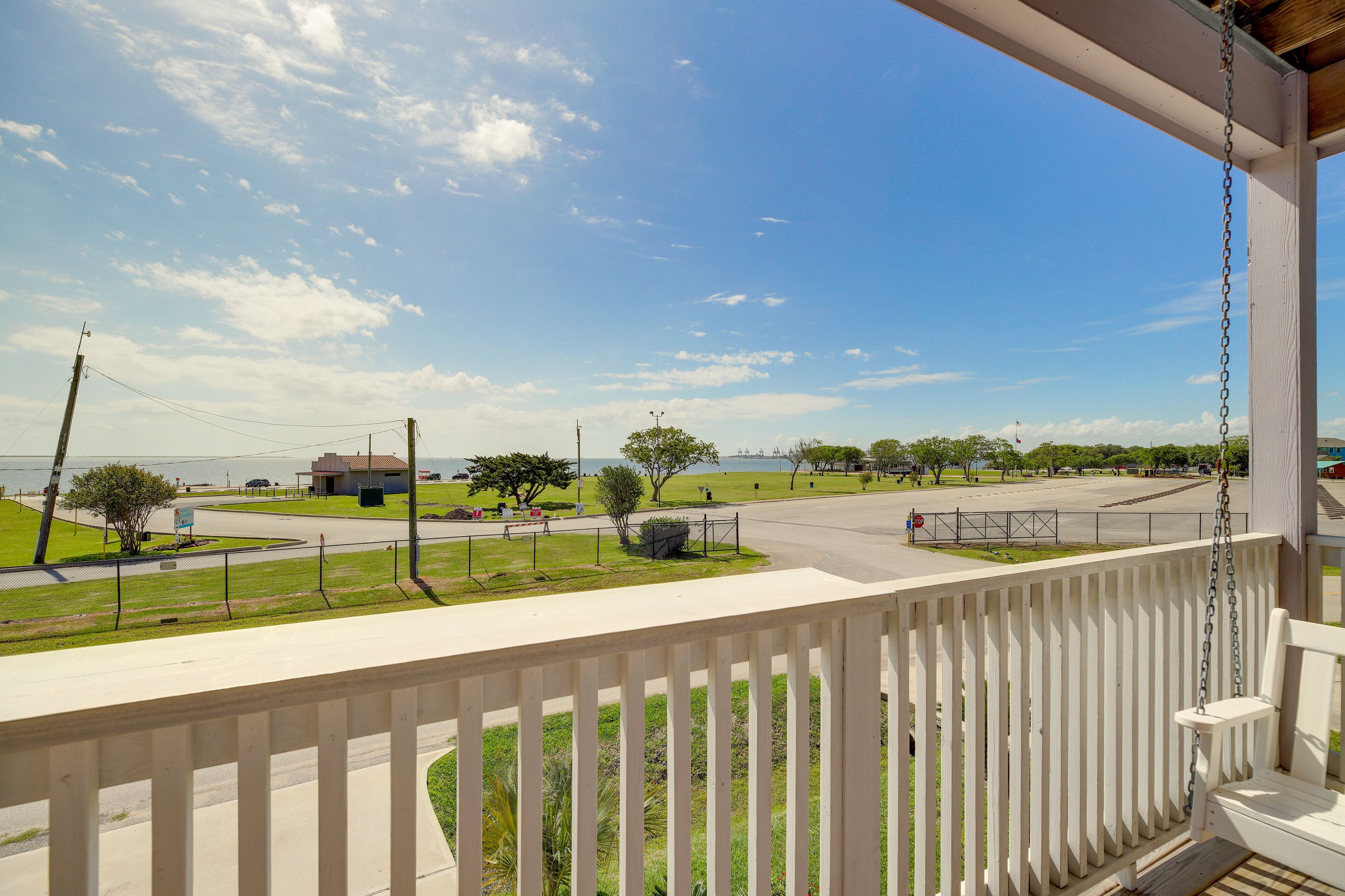 A balcony with a view of a parking lot, grassy areas, and a distant body of water.