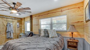 A bedroom with a large bed, wooden walls, a ceiling fan, a window with blinds, and a bedside table with a lamp. - Farm Stay: Modern Barndominium in Lakeland! (Lakeland)