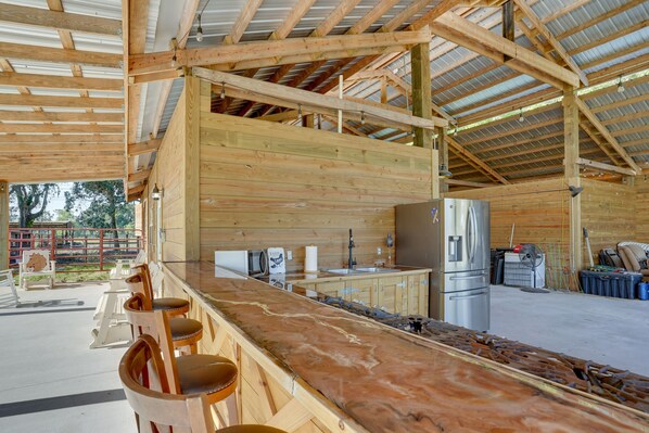 A spacious kitchen with wooden cabinets, a stainless steel refrigerator, and a long counter with bar stools.
