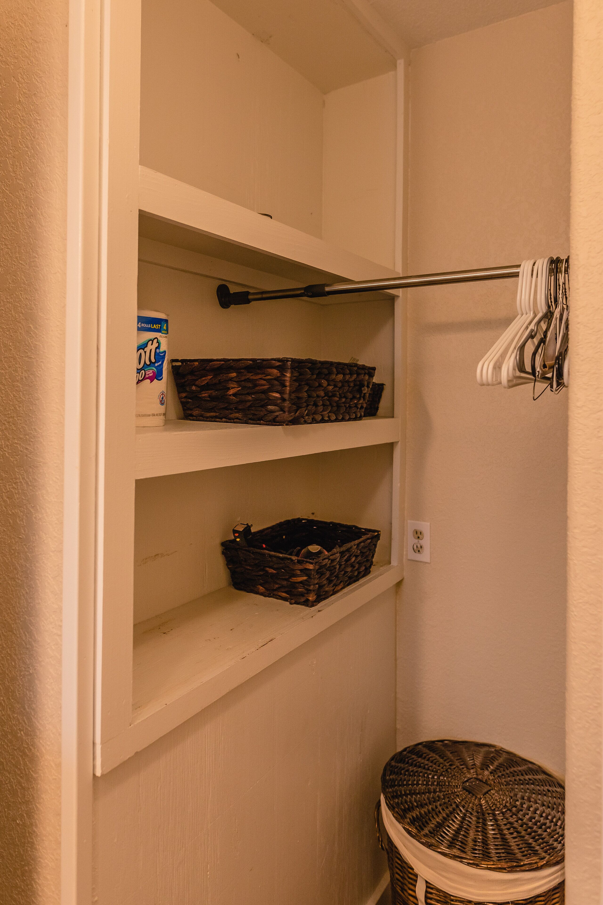 A small storage closet with shelves, a hanging rack, and a round wicker basket.