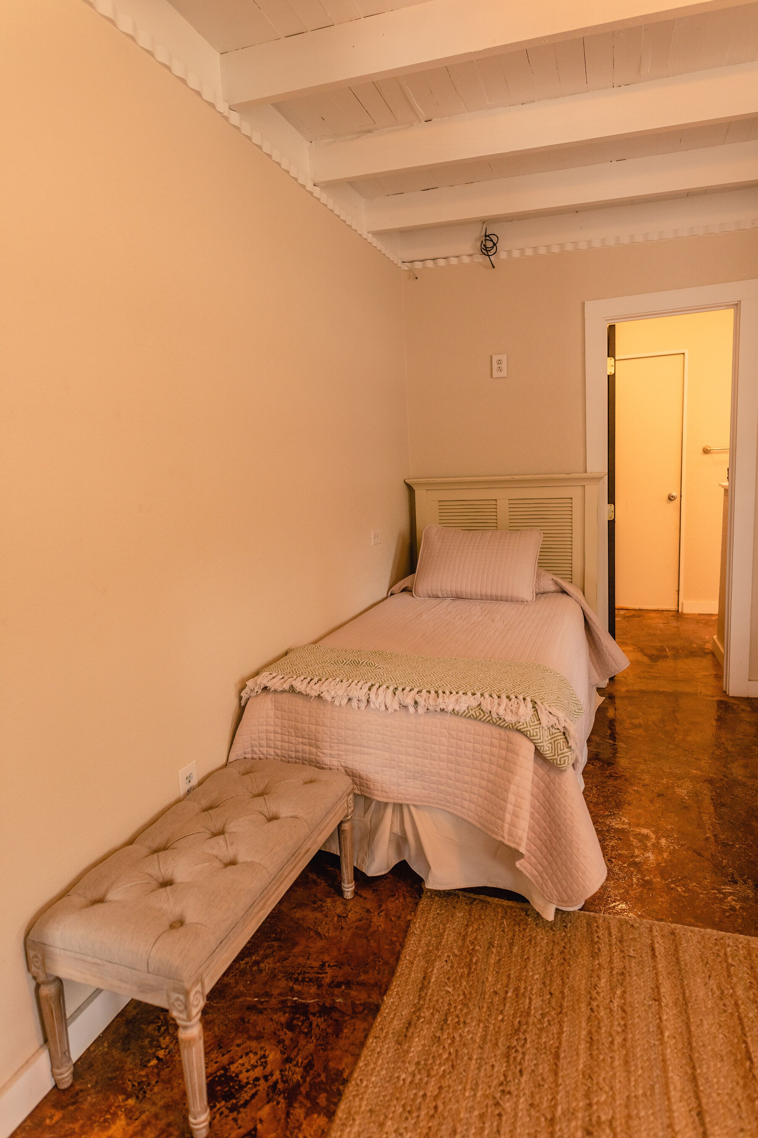 A bedroom with a bed, bench, and a door leading to another room.