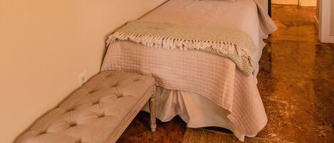 A bedroom with a bed, bench, and a door leading to another room.