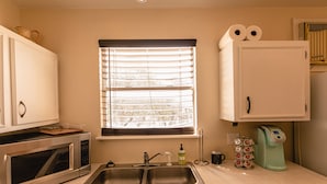 A kitchen with a double sink, a microwave, a coffee maker, and a window with blinds.