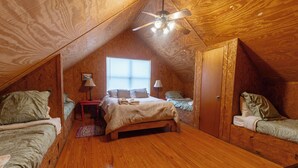 A cozy attic bedroom with a wooden ceiling, a bed with a beige blanket, two bedside tables with lamps, and a window providing natural light. - Located 1/4 Mile to River Access (Concan)