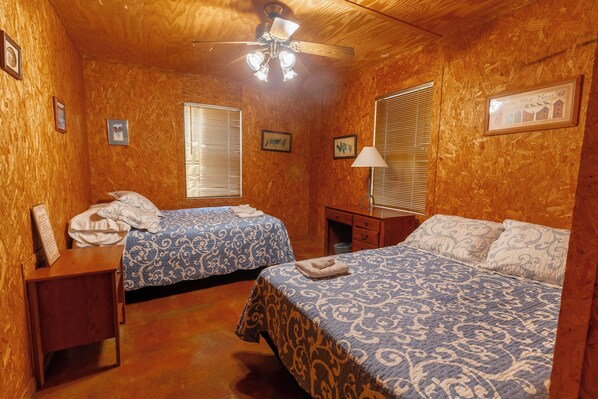 A room with two beds, wooden walls, a ceiling fan, and framed pictures on the walls.