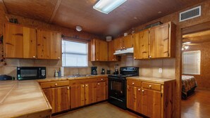 A kitchen with wooden cabinets, a microwave, stove, and a sink. - Located 1/4 Mile to River Access (Concan)