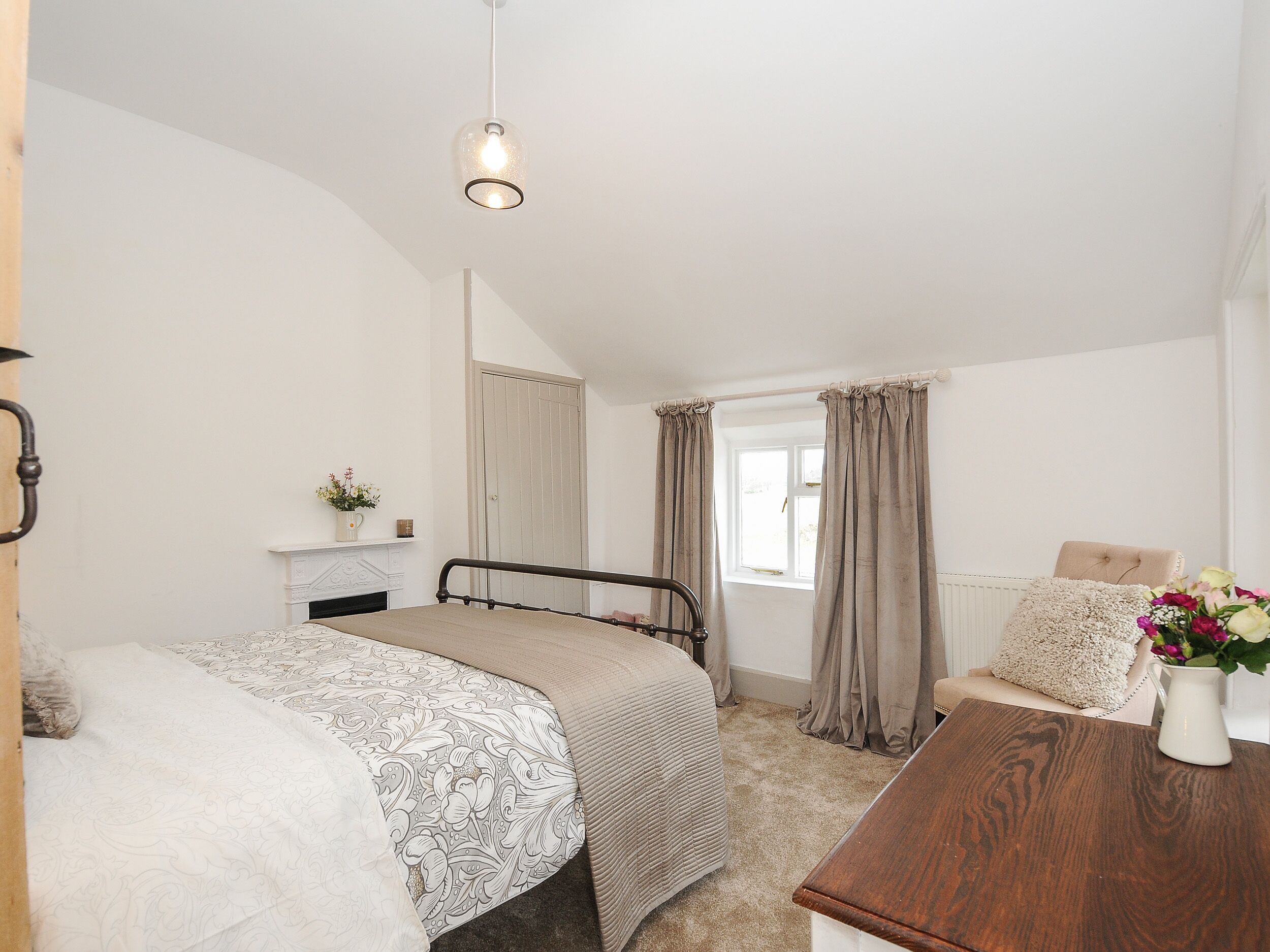 A bedroom with a bed, a wooden nightstand, a window with curtains, and a hanging light fixture.