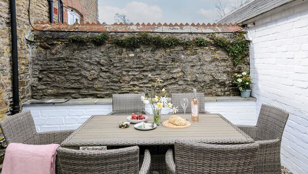 Une terrasse extérieure avec des meubles en osier, une table dressée avec de la nourriture et des boissons, et un mur de pierre en arrière-plan.