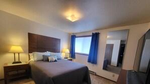 Ein Hotelzimmer mit einem großen Bett, zwei Nachttischen mit Lampen, einem Spiegel und einem Fenster mit Vorhängen.