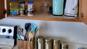 Eine Küche mit Holzböden, die Gewürze, einen Wasserkocher und eine Kaffeemaschine beherbergen. Darunter befinden sich Kochutensilien und Behälter.