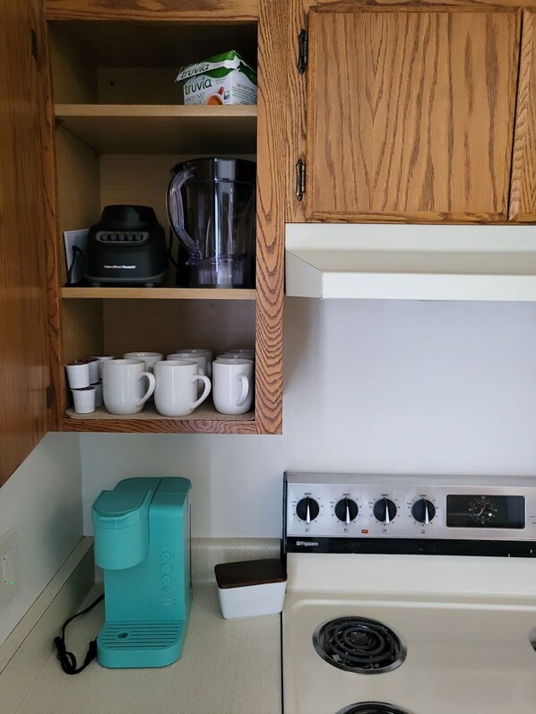 Una cocina compacta con armarios de madera, una licuadora Hamilton Beach, una estufa Frigidaire y una cafetera color esmeralda.