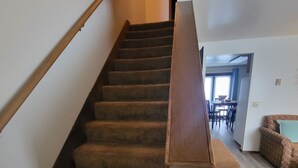 Eine Treppe mit Teppichstufen und Holzhandläufen, die zu einem Raum mit hellem Boden und einem Essbereich im Hintergrund führt.