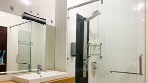 Ein modernes Badezimmer mit einem großen Spiegel, einem weißen Waschbecken und einer gläsernen Dusche.