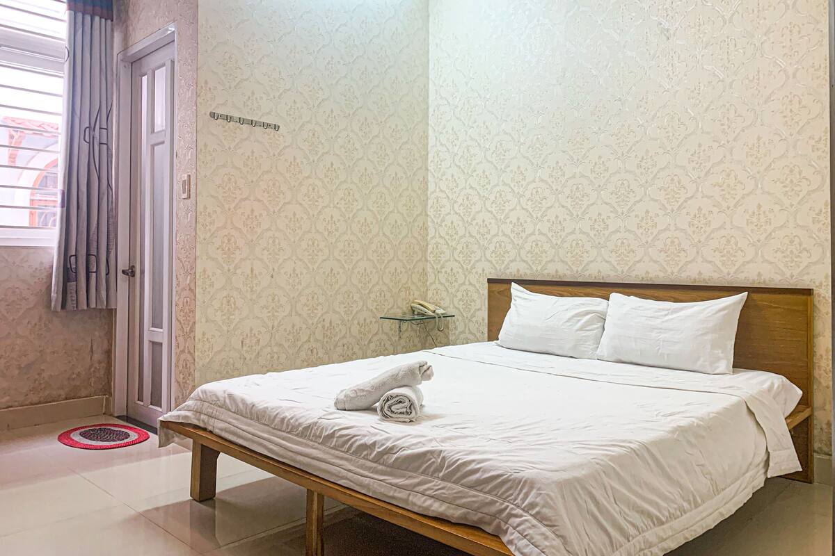 Un lit bien fait, avec des draps blancs, une tête de lit en bois et une serviette enroulée posée sur le lit.