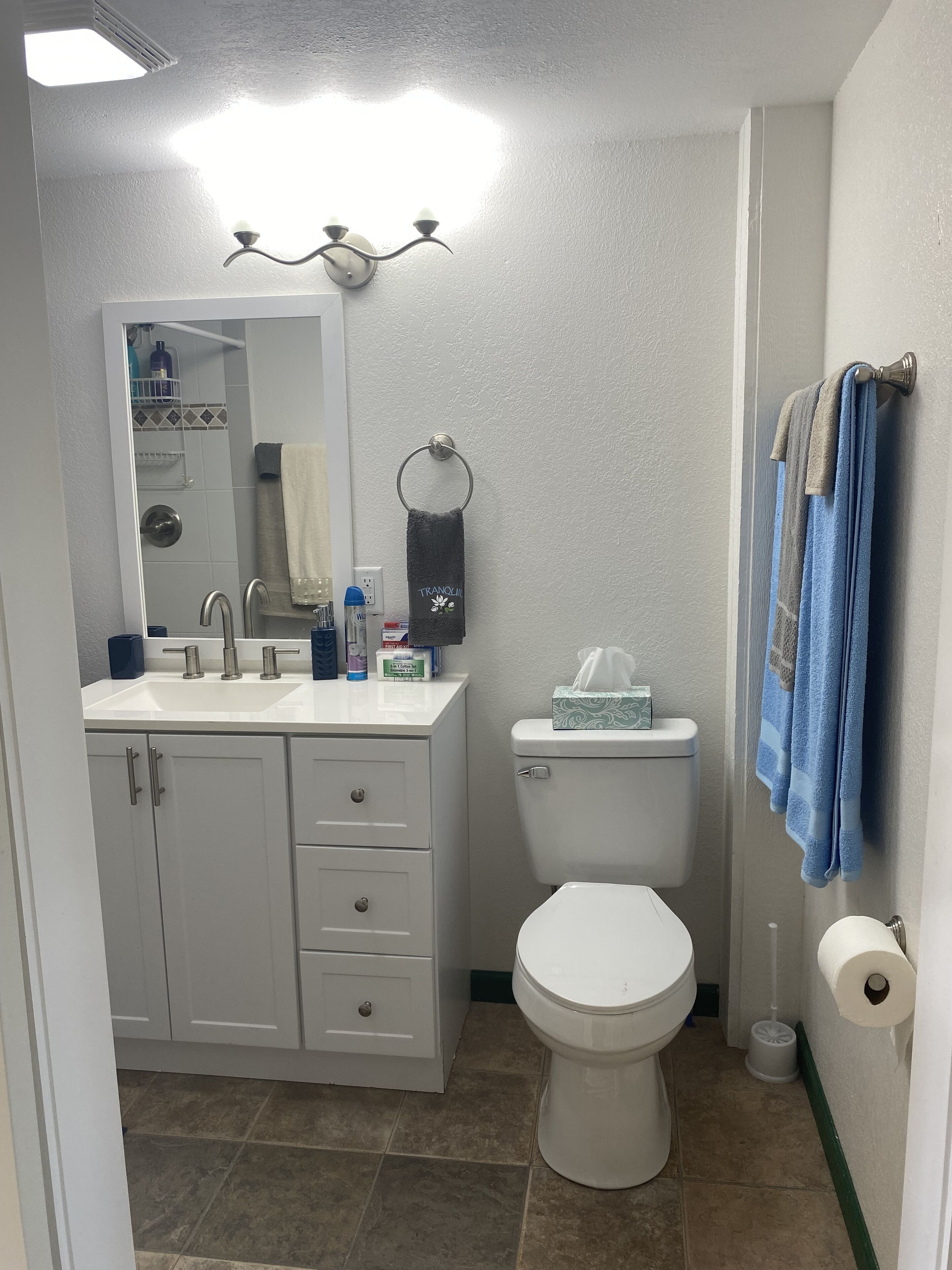 Un baño con un lavabo blanco, un inodoro y un espejo. Hay toallas colgadas en la pared y una cortina de ducha en el fondo.