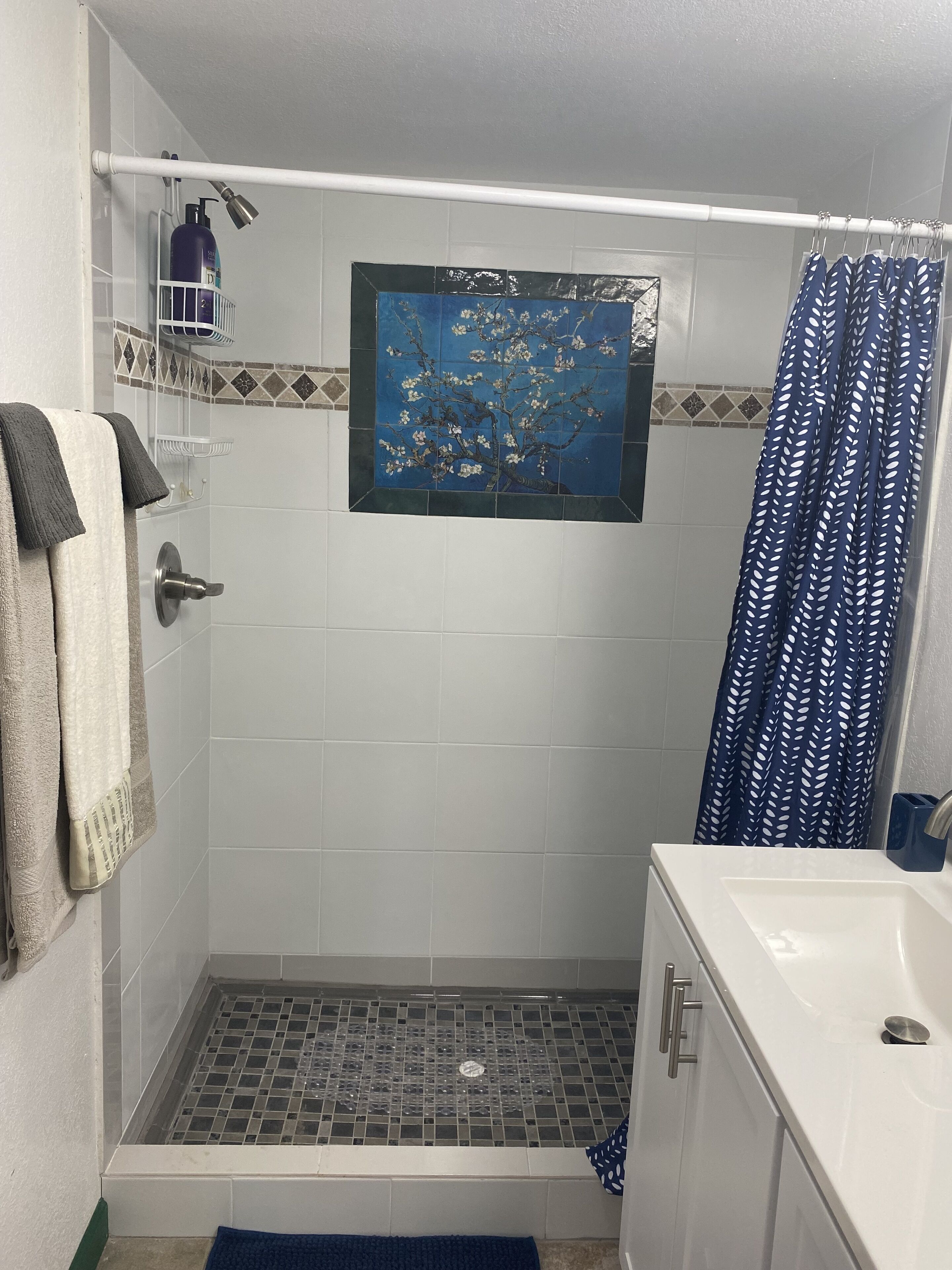 Eine Dusche mit blau gefliestem Blumenfries, einer weißen Badewanne und einem blauen Duschvorhang mit weißen Mustern.