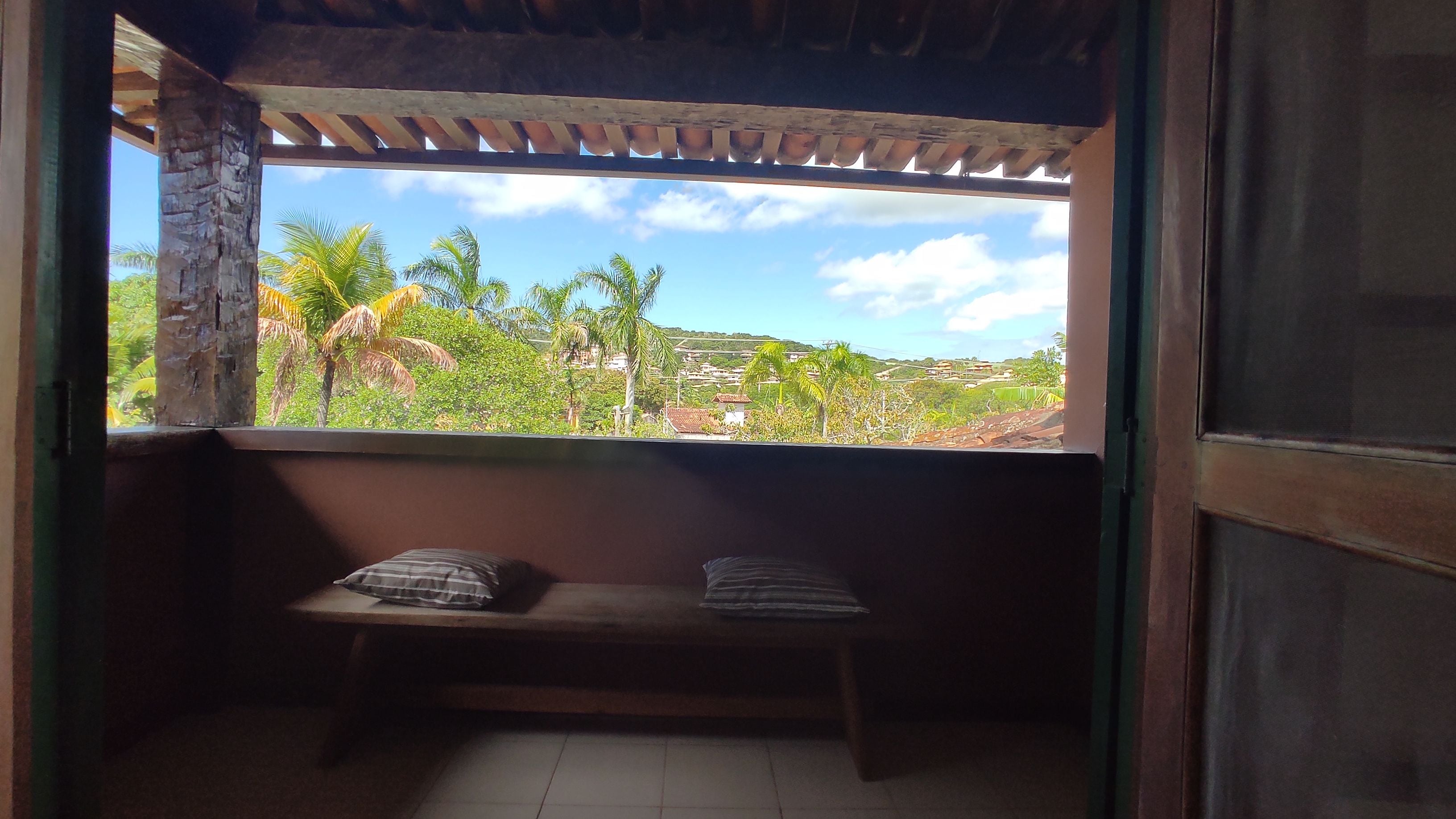 A room with a window overlooking a landscape with palm trees and buildings.