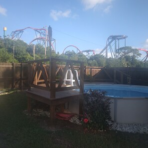Eine Holzterrasse mit einem weißen Stuhl, einem Schwimmbecken und Achterbahnstrecken im Hintergrund.
