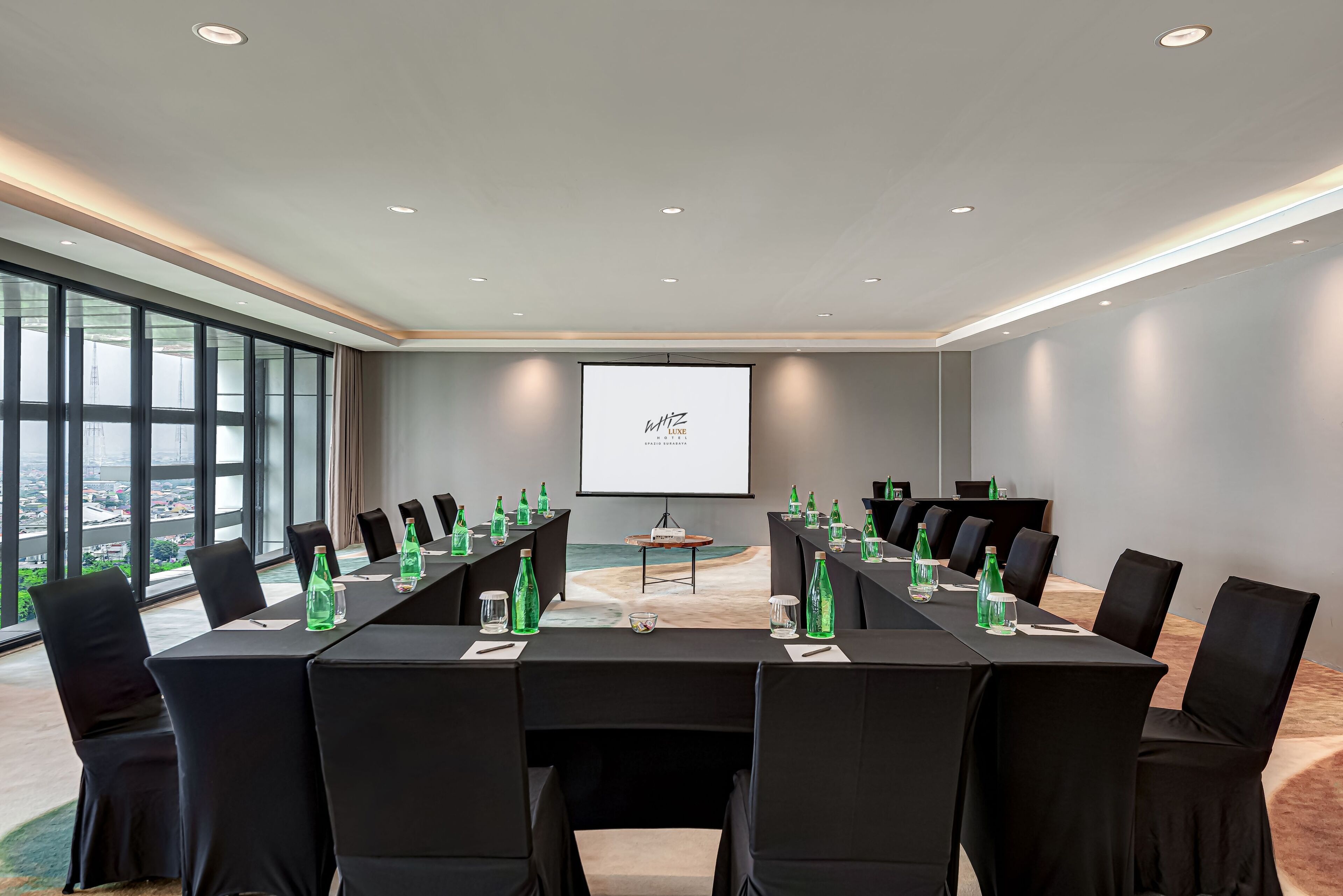 Un salón de conferencias con una larga mesa, sillas negras y una pantalla de proyector.