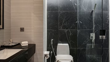 Un bany modern amb dutxa de marbre negre, vàter blanc i una superfície de taula negra amb un rentapelats i productes de tocador.