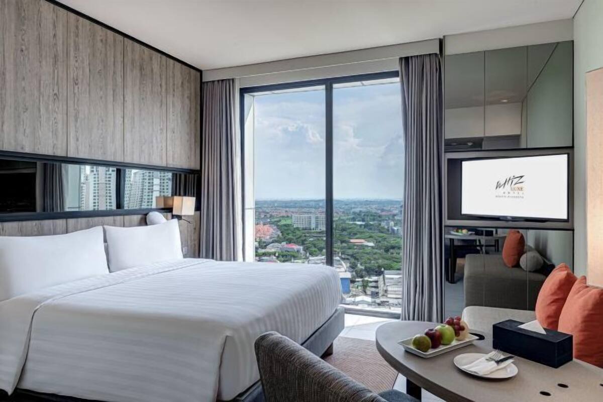Une chambre d’hôtel moderne avec un grand lit, un coin repas avec une table dressée pour deux personnes et un téléviseur.