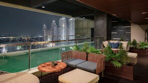Une terrasse sur le toit avec une piscine, des meubles en osier et une vue sur la ville la nuit.