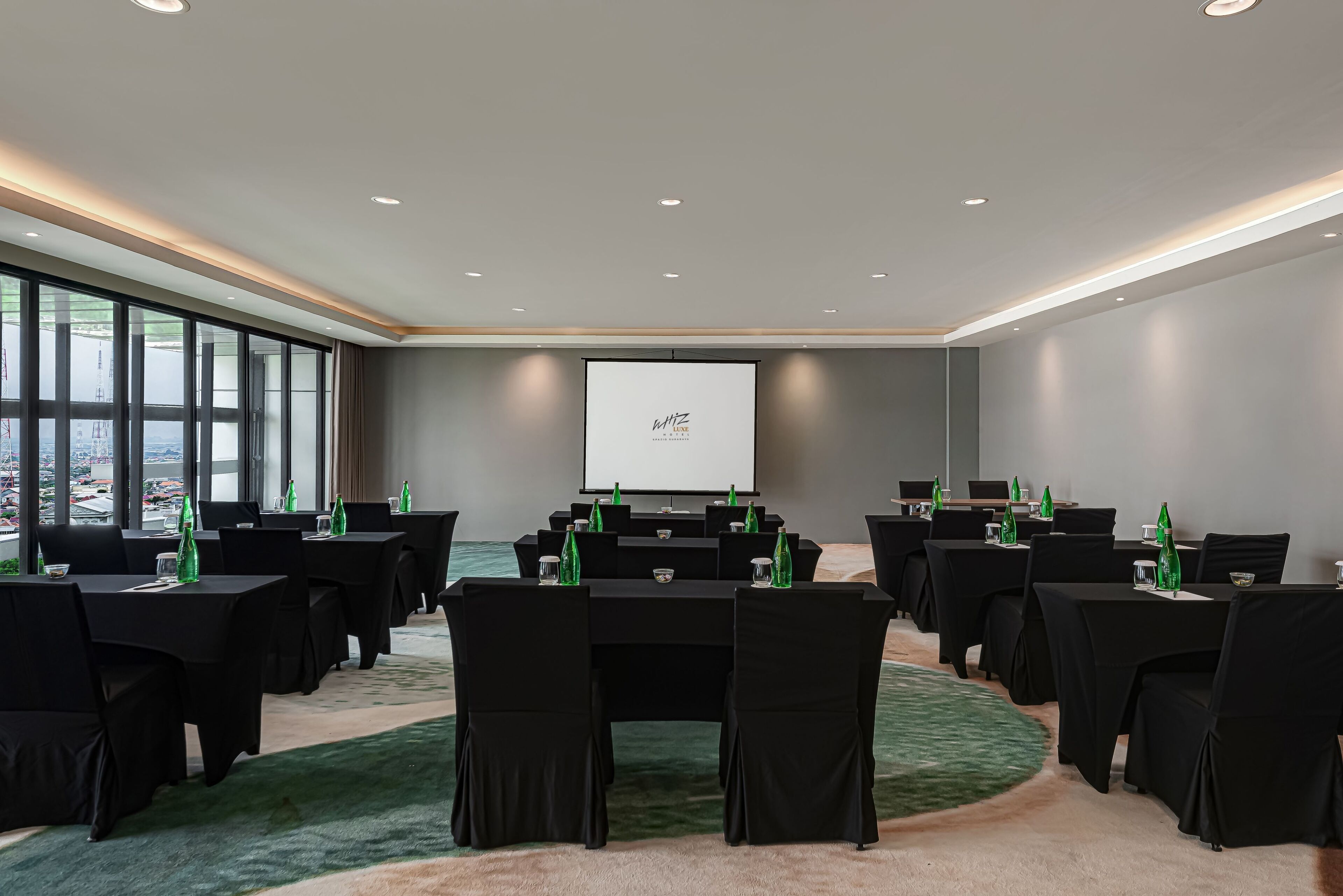 A conference room with black tables and chairs, a projector screen, and a carpeted floor.